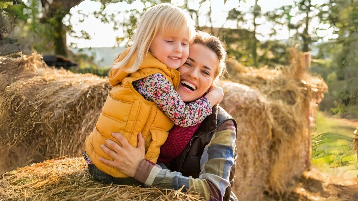 a mom and girl child sitting on a pile of hay