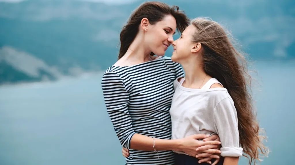 a mother and daughter hugging in front of the ocean