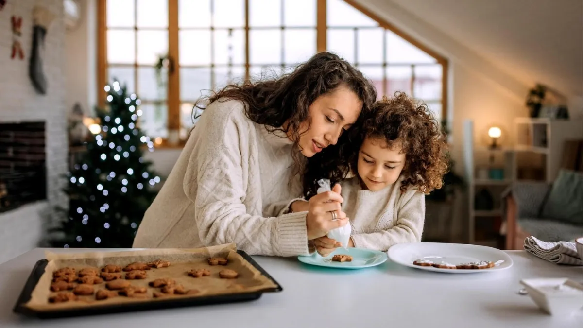 mother and daughter eating cookies in front of christmas tree